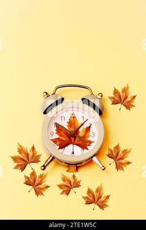Wecker umgeben von Herbstahornblättern auf gelbem Hintergrund Stockfoto