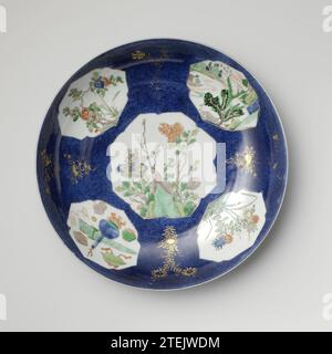 Untertasse mit Puderblau und Platten in Reserve mit Blumensprays, Landschaften und kostbaren Gegenständen, anonym, ca. 1700 - ca. 1724 Schale mit runder Porzellanwand, bemalt in Unterglasur blau und auf der Glasur blau, rot, grün, gelb, Aubergine, schwarz und Gold. Die Vorder- und Rückseite des Gerichts sind mit blauem Poudré (pulverblau) bedeckt, wobei fünf Kartuschen gerettet sind; auf der Ebene ein Felsen mit Birnzweigen; an der Wand ein prunus-Zweig, eine Flusslandschaft, ein Blumenzweig und Antiquitäten und Wertsachen (Vase, artemisia-Blatt), dazwischen eine Blume in Gold auf dem Blau; die Rückseite mit abgetragenem flo Stockfoto