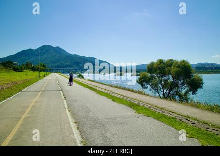 Namyangju City, Südkorea - 30. September 2023: Wanderer auf dem Han River Radweg in Namyangju, wobei die ferne Paldang-Brücke subtil den Fluss verstärkt Stockfoto