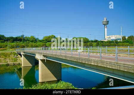 Namyangju City, Südkorea - 30. September 2023: Der beschauliche Wangsuk Stream fließt sanft unter einer niedrigen Fußgängerbrücke mit dem majestätischen Guri Tower Stockfoto