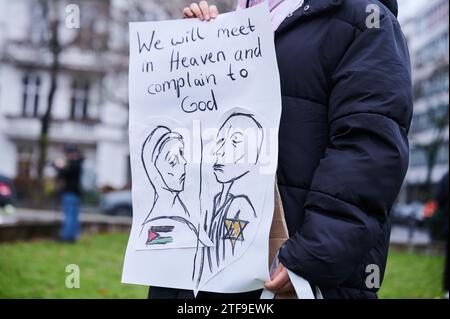 20. Dezember 2023, Berlin: "Wir werden uns im Himmel treffen und uns bei Gott beschweren" steht über einer Zeichnung einer trauernden Frau mit palästinensischer Flagge auf der einen Seite und einem "Holocaust-Überlebenden-Juden" (Zitat des Demonstrators) auf der anderen Seite. Der Demonstrant und Illustrator nimmt am Steinplatz unter dem Motto "Studenten vereint für ein freies Palästina" Teil. Die Berliner Studentenvereinigung hat zur Demonstration aufgerufen, die sich gegen Israels Angriffe auf den Gazastreifen richtet. Die Organisatoren werfen Israel vor, für den Völkermord an Palästinensern verantwortlich zu sein. Foto: Annette Riedl/dpa Stockfoto