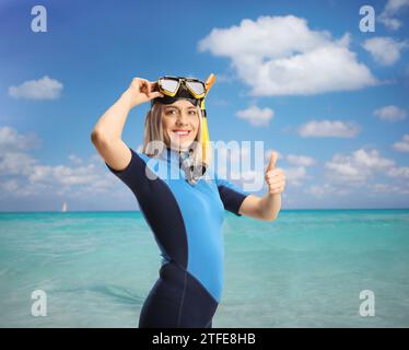 Frau in einem Nassanzug mit einer Tauchmaske, die die Daumen auf dem Meer nach oben drückt Stockfoto