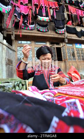 (231220) -- LONGSHENG, 20. Dezember 2023 (Xinhua) -- Eine Frau demonstriert die Nähtechnik der Volkstrachten der Hongyao während des Festivals „Trocknen der Kleidung“ im Dorf Dazhai in Longji, County Longsheng, südchinesische Autonome Region Guangxi Zhuang, 2. Juli 2014. Die Menschen von Hongyao, einem Zweig der Yao-ethnischen Gruppe, leben seit Generationen im Longsheng County von Guangxi. Die Volkskostüme der Hongyao sind in der Farbe Rot gehalten und mit zarten Herstellungstechniken versehen. Sie sind charakteristisch für den Zweig der ethnischen Gruppe der Yao. Während des jährlichen „Trocknens von Kleidung“ Stockfoto