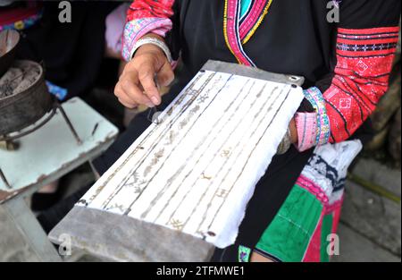 (231220) -- LONGSHENG, 20. Dezember 2023 (Xinhua) -- Eine Frau demonstriert die Wachsdrucktechnik von Volkstrachten der Hongyao während des Festivals „Trocknen von Kleidung“ im Dorf Dazhai in Longji, County Longsheng, südchinesische Autonome Region Guangxi Zhuang, 2. Juli 2014. Die Menschen von Hongyao, einem Zweig der Yao-ethnischen Gruppe, leben seit Generationen im Longsheng County von Guangxi. Die Volkskostüme der Hongyao sind in der Farbe Rot gehalten und mit zarten Herstellungstechniken versehen. Sie sind charakteristisch für den Zweig der ethnischen Gruppe der Yao. Während des jährlichen Trocknungstuches Stockfoto