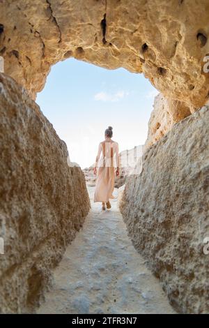 Reise durch den Natural Bogenway: Eine vertikale Aufnahme einer Frau in einem fließenden Kleid, die von der Kamera weggeht Stockfoto