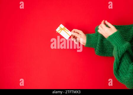 Weihnachtseinkaufskonzept. Flache Hände in einem grünen Pullover mit Bonuskarte. Banner auf rotem Hintergrund Stockfoto