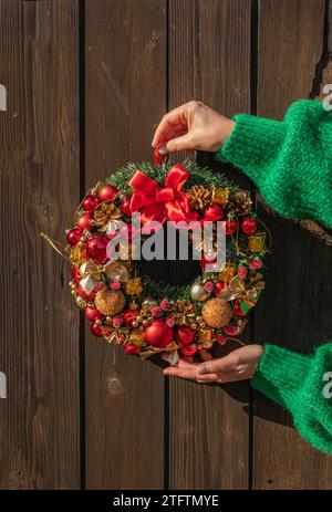 Frauenhände in grünem Pullover, der den Tannenkranz für den Advent aufhängt. Heiligabend und Dekoration. Neujahrsfeier. Stockfoto