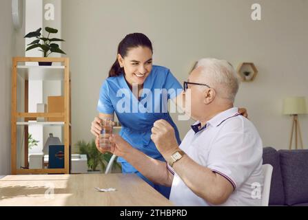 Freundliche junge Krankenschwester, die Senioren im Pflegeheim Medikamente und ein Glas Wasser gibt. Stockfoto