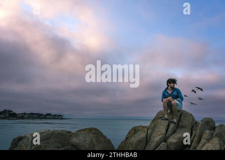 Ein junger Mann, der die Vögel am Rocky Edge des Lovers Point Park - Pacific Grove, Kalifornien, beobachtet Stockfoto