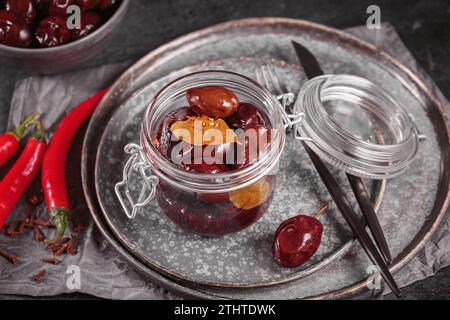 Marinierte Pflaumen mit Gewürzen im Glasgefäß auf dem Küchentisch Stockfoto