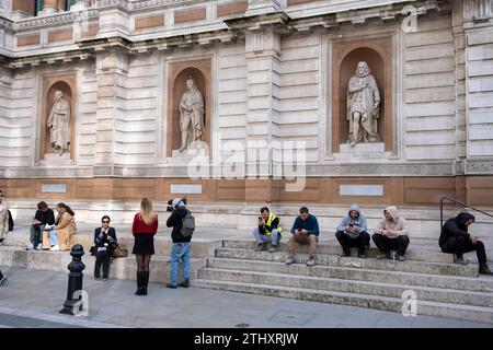 Menschen interagieren mit Statuen bekannter Männer vor der Royal Academy of Arts am 16. Oktober 2023 in London, Großbritannien. Die Gegenfiguren stellen eine Gegenüberstellung der sehr unterschiedlichen Epochen dar. Stockfoto