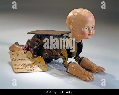 Mechanisch kriechende Babypuppe, 1871, Patent Nr. 118435, erfunden von George P. Clarke. Dieses Modell demonstriert die Erfindung einer mechanischen Kriechpuppe, die am 29. August 1871 das US-Patent Nr. 118435 für seine ÒNatural Kriechbaby Doll Ó erhielt. Das Original-Patent-Büroschild ist noch immer mit rotem Klebeband befestigt. Clarkes Patent war eine Verbesserung des Crawling Baby Puppe Patents seines Kollegen Robert J. Clay (Nr. 112550 erteilt am 14. März 1871). Optimierte Version eines Bildes eines Objekts im Smithsonian American Art Museum, Washington DC, USA. Stockfoto
