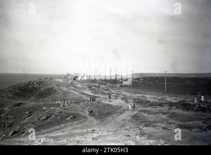 Um die 1940er Jahre, historisches Bild von Lands End, Cornwall, England, zeigt Menschen auf dem felsigen Gelände der Küste und in der Ferne das berühmte „First & Last House in England“, ein altes Cottage, das Souvenirs und Erfrischungen an die Besucher verkaufte. Stockfoto