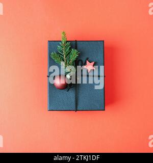 Schwarze Geschenkbox mit Weihnachtsdekoration auf rotem Hintergrund. Draufsicht, flach. Stockfoto