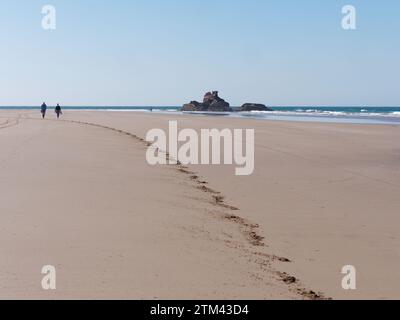 Ein paar Leute spazieren an einem Sandstrand mit Felsvorsprüngen in der Stadt Essaouira, der „windigen Stadt“, Marokko. Dezember 2023 Stockfoto