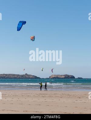 Kitesurfer mit einer Insel dahinter an einem Sandstrand in der Stadt Essaouira, der „windigen Stadt“, Marokko. Dezember 2023 Stockfoto