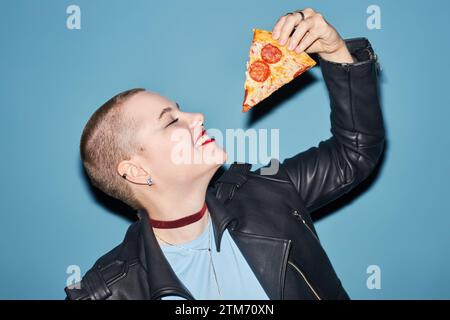 Fröhliche junge Frau, die ein Stück Pizza hält Stockfoto