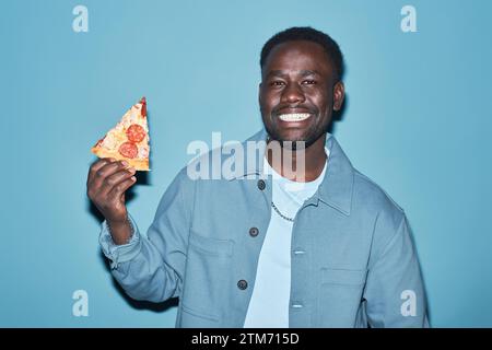 Glücklicher junger Schwarzer, der ein Stück Pizza hält Stockfoto