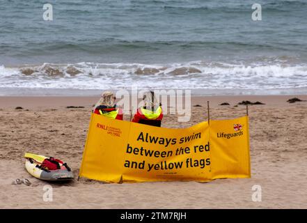 RNLI Rettungsschwimmer am Strand von Tenby Pembrokeshire Wales sitzen hinter Windschutzscheiben und schwimmen zwischen den roten und gelben Fahnen. Stockfoto