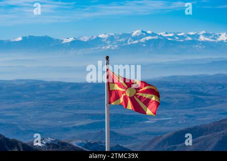 mazedonische Flagge auf Silberpfosten schwenken. Hoch am Himmel. Oberhalb des Berghügels. Rote und gelbe Farben. Gefrorener Peak im Hintergrund. Ponikva Mazedonien Stockfoto