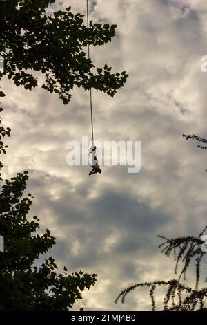 Ein Mann, der kopfüber an ein Seil gebunden ist, macht einen Bungee-Sprung, während er eine Action-Kamera hält Stockfoto