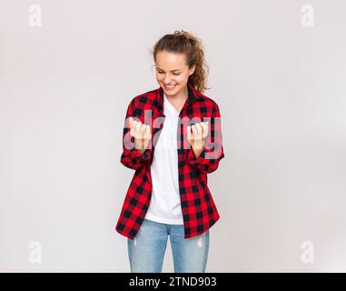 Frau in lässigem Outfit, die auf ihre Nägel schaut und vor einem schlichten Hintergrund im Studio lächelt. Stockfoto