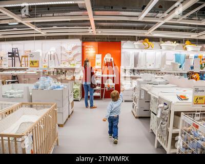 Paris, Frankreich - 31. August 2023: Ungeduldiges Kleinkind zeigt auf Kinderaccessoires und Pflegeobjekte in IKEA, während Mutter auf einen Kinderstuhl blickt Stockfoto