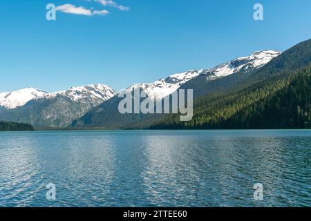 Die beschauliche Weite des Cheakamus Lake spiegelt die umliegenden schneebedeckten Berge unter dem weitläufigen blauen Himmel von British Columbia wider. Stockfoto