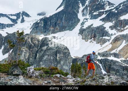 Ein einsamer Wanderer durchquert das zerklüftete alpine Gelände der Kanadischen Rocky Mountains, umgeben von majestätischen schneebedeckten Gipfeln. Stockfoto