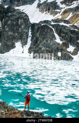 Ein überschwänglicher Wanderer feiert die eisige Weite des Wedgemount Lake inmitten der kanadischen Gipfel. Stockfoto