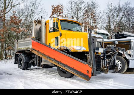 Industrieller gelber leistungsstarker Kipper mit Day Cab, großer Lkw-Sattelzugmaschine mit Schneeschaufel und kompakter Muldenkipper, die auf dem Wintereinsatz in Reihe steht Stockfoto