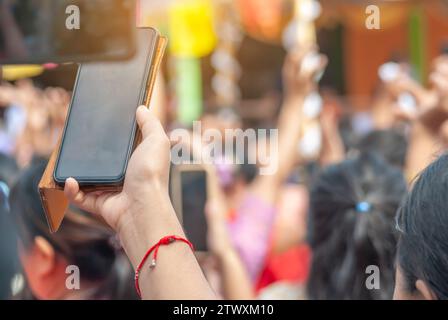 Handfrauen, die ein Smartphone halten, um burmesische Menschen in nationalen Kostümen zu erschießen, kommen Sie heraus, um am Kathin Festival teilzunehmen und zu tanzen Stockfoto