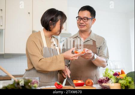 Ein fürsorglicher asiatischer Ehemann hilft seiner Frau, in der Küche zu frühstücken, und verbringt gemeinsam zu Hause gute Zeit. Schönes erwachsenes Paar, Hausmannskost, Stockfoto