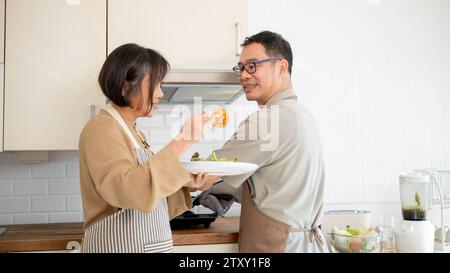 Ein hübsches asiatisches Paar genießt das Essen nach dem Kochen in der Küche und verbringt am Wochenende eine gute Zeit zu Hause. Erwachsene Paare Stockfoto