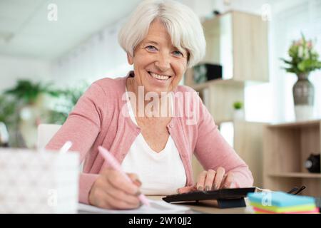 Seniorin mit Taschenrechner und Rechnungen, die zu Hause Geld zählen Stockfoto