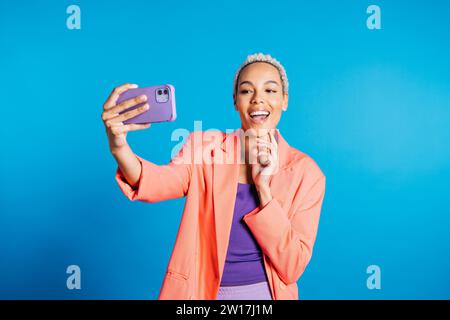 Glückliche junge Frau, die ein Selfie vor blauem Hintergrund in einem Studio macht. Eine Frau, die ein Selfie in einem Studio macht. Stockfoto