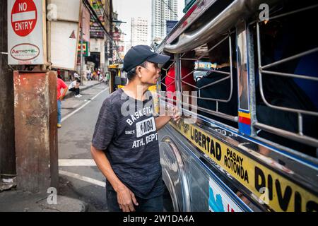 Ein philippinischer Mann läuft an der Seite eines Jeepney entlang. Ich bin mir ehrlich nicht sicher, ob er Geld für Fahrgeschäfte oder Betteln sammelte. Stockfoto