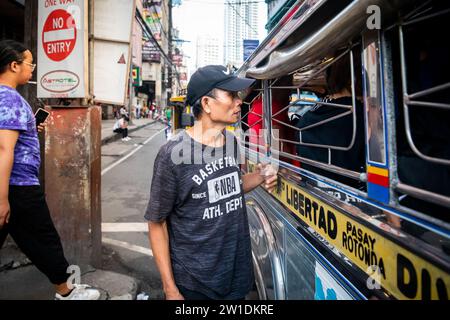 Ein philippinischer Mann läuft an der Seite eines Jeepney entlang. Ich bin mir ehrlich nicht sicher, ob er Geld für Fahrgeschäfte oder Betteln sammelte. Stockfoto