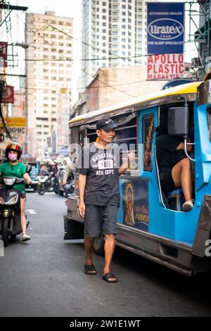 Ein philippinischer Mann läuft an der Seite eines Jeepney entlang. Ich bin mir ehrlich nicht sicher, ob er Geld für Fahrgeschäfte oder Betteln sammelte. Stockfoto