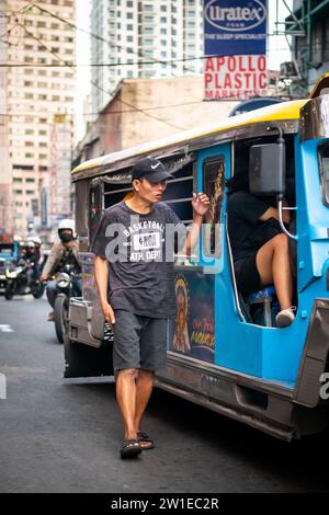 Ein philippinischer Mann läuft an der Seite eines Jeepney entlang. Ich bin mir ehrlich nicht sicher, ob er Geld für Fahrgeschäfte oder Betteln sammelte. Stockfoto