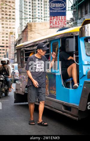 Ein philippinischer Mann läuft an der Seite eines Jeepney entlang. Ich bin mir ehrlich nicht sicher, ob er Geld für Fahrgeschäfte oder Betteln sammelte. Stockfoto