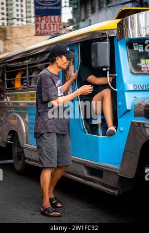 Ein philippinischer Mann läuft an der Seite eines Jeepney entlang. Ich bin mir ehrlich nicht sicher, ob er Geld für Fahrgeschäfte oder Betteln sammelte. Stockfoto