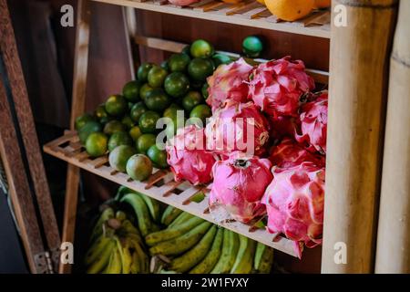 Entdecken Sie den exotischen Reiz von Drachenfrüchten, leuchtenden grünen Limetten und Reifen Bananen, die harmonisch auf einem Holzregal in einem umweltfreundlichen Geschäft angeordnet sind. Stockfoto