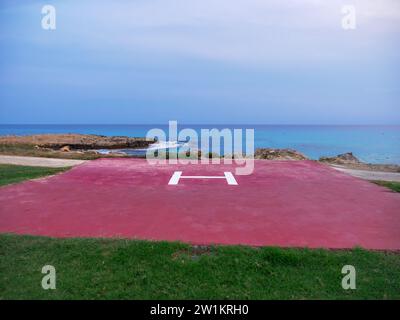 Roter Hubschrauberlandeplatz mit einem H-Buchstaben in der Mitte am Ufer des Mittelmeers mit Blick auf das Meer und grünem Rasen im Vordergrund. Stockfoto