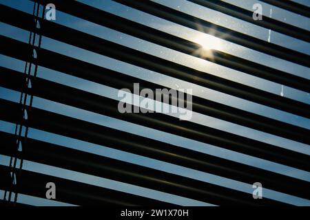 Jalousien am Fenster zum Schutz vor Sonnenlicht. Nahaufnahme von modernem Jalousie. Blick auf die Sonnenstrahlen durch Holzjalousien Stockfoto