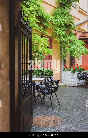 Gemütliches Straßencafé mit Eisenzaun in der Altstadt. Leere Terrasse mit Gartenmöbeln und roten Blumen. Hotelterrasse mit Stühlen und Tischen. Straßencafé Stockfoto