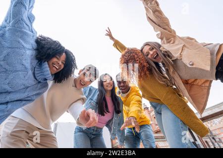 Jugendliche Freunde zeigen in einem lebhaften Selfie, voller Vitalität und verspielter Gesten unter hellem Himmel die Hände zur Kamera Stockfoto