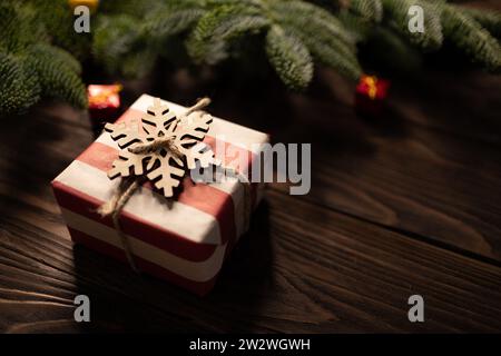 Weihnachtsgeschenk in gestreiftes Bastelpapier gewickelt und mit Holzschneeflocke auf hölzernem Hintergrund verziert, eingerahmt von edlen Tannenzweigen Stockfoto