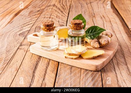 Natürliches hausgemachtes Ingwerwurzelöl in zwei Glasflaschen mit Korkdeckel auf einem Holzschneidebrett mit Ingwerwurzelscheiben. Multivitamine. Stockfoto