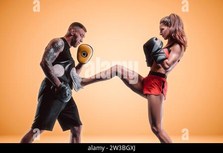 Sportliche Frau in roten Shorts und Oberteil boxt mit einem Trainer. Boxen und Mixed Martial Arts Konzept. Gemischte Medien Stockfoto